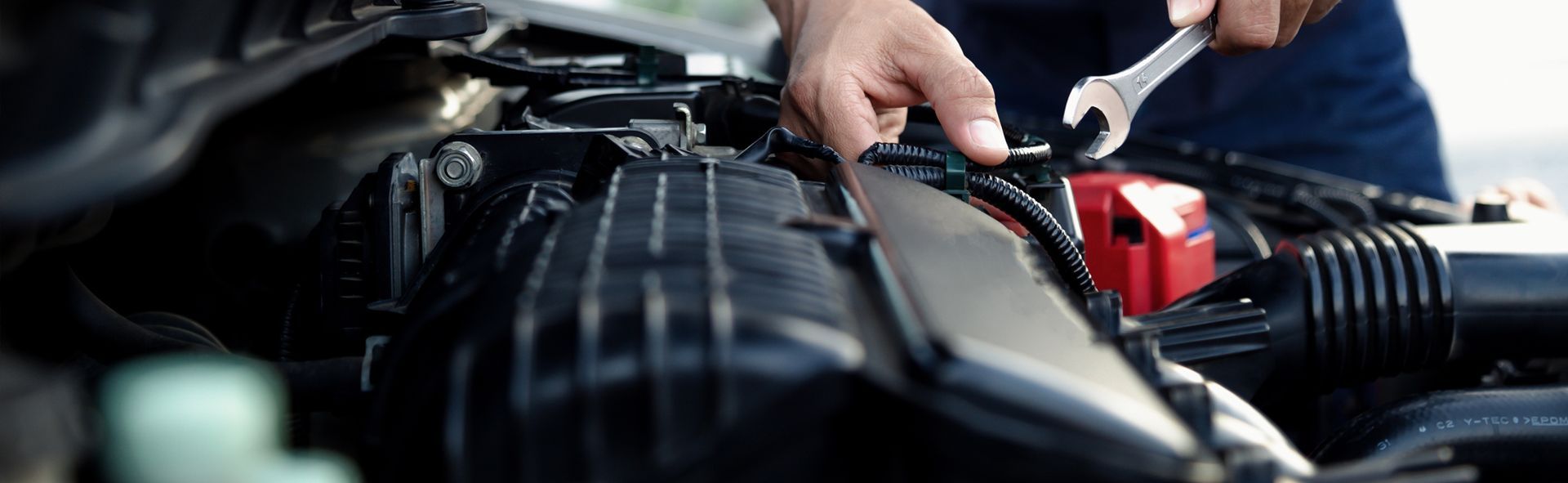 Mechanic working on a car engine with a wrench. Black engine components and a red battery.