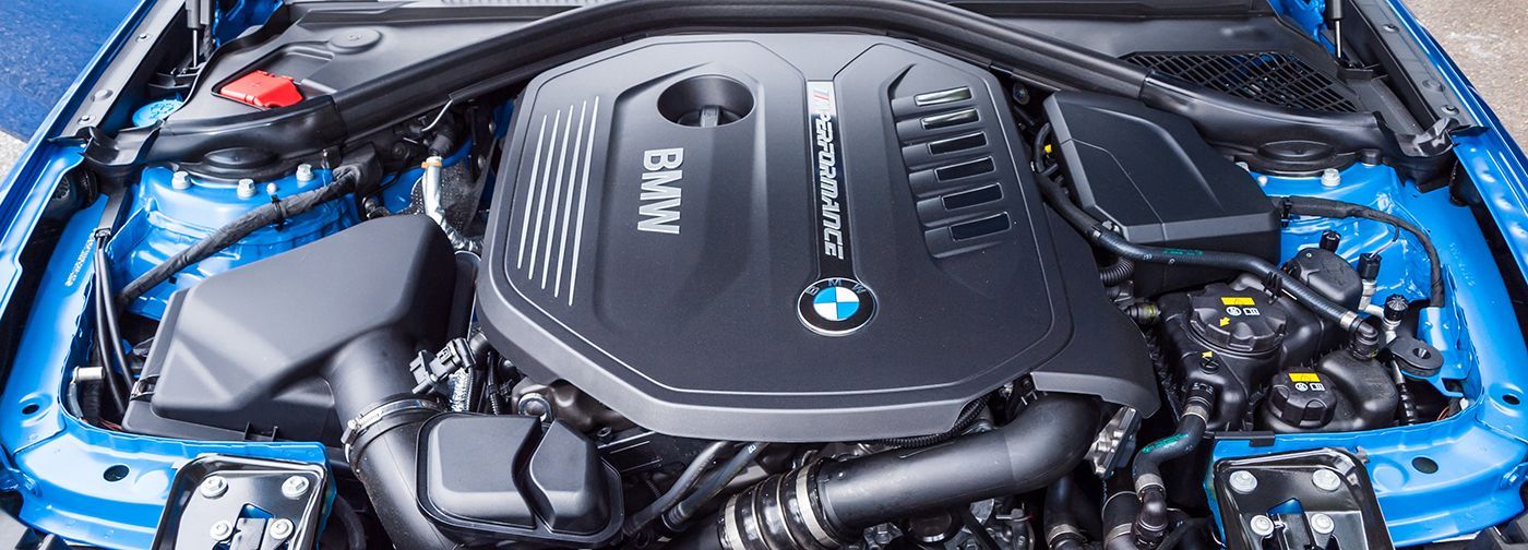 The blue engine bay of a BMW car, featuring a black engine cover with the BMW logo in the center.