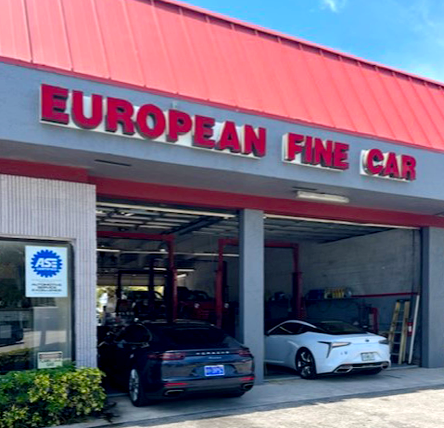 Two cars are parked in front of a building that says european fine car