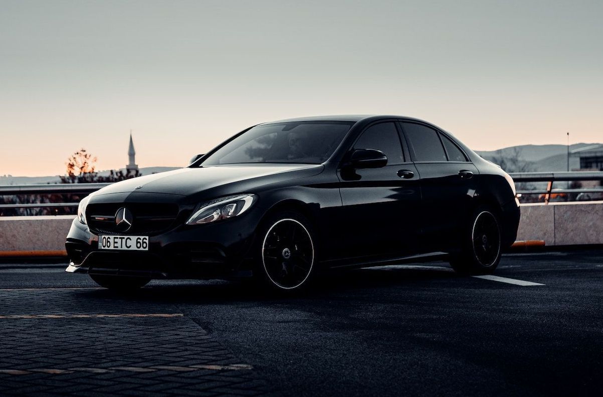 A black mercedes benz is parked in a parking lot.