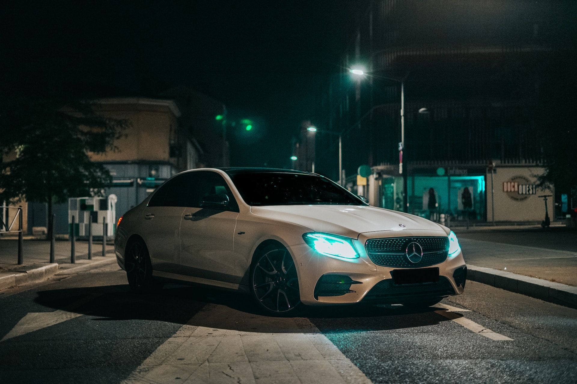 A white mercedes benz is driving down a city street at night.