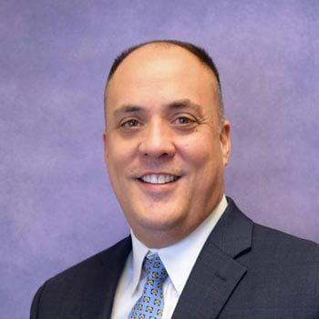 Man in suit smiling, indoors, on purple background.