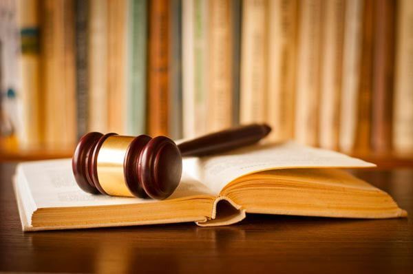 Gavel resting on an open book, with a blurred background of bookshelves.