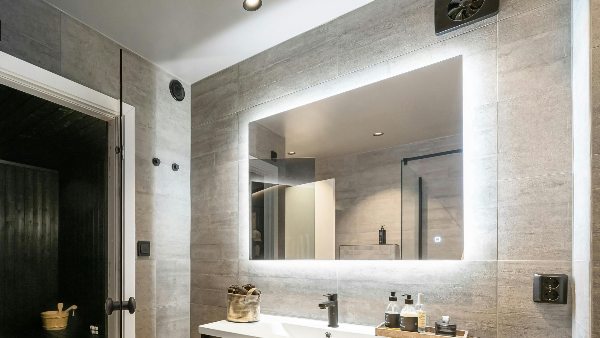 Modern white bathroom with double vanity, freestanding tub, and glass-enclosed shower under black tile floor