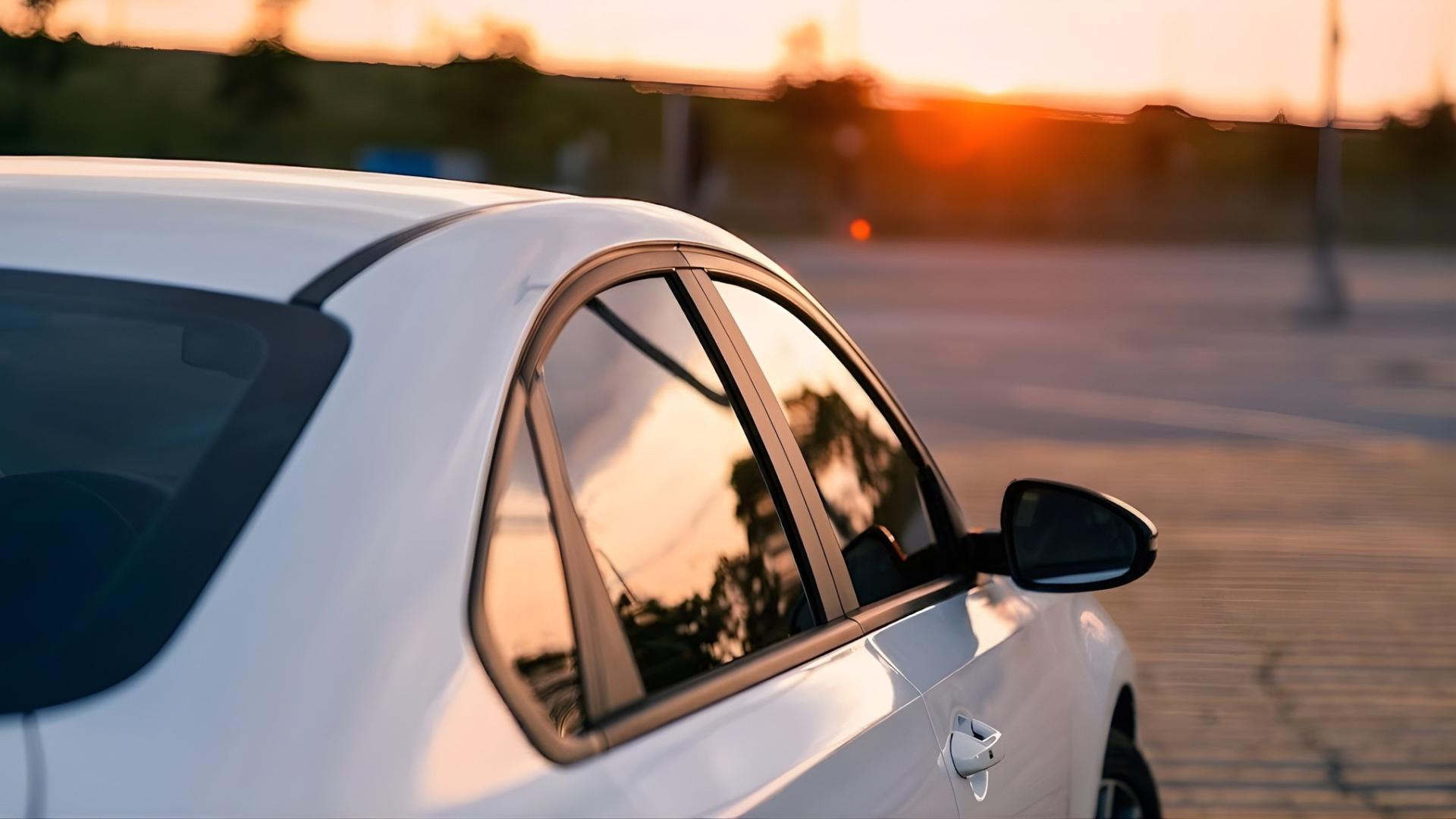 White sedan at sunset with tinted rear window, parked in an open lot near the horizon.
