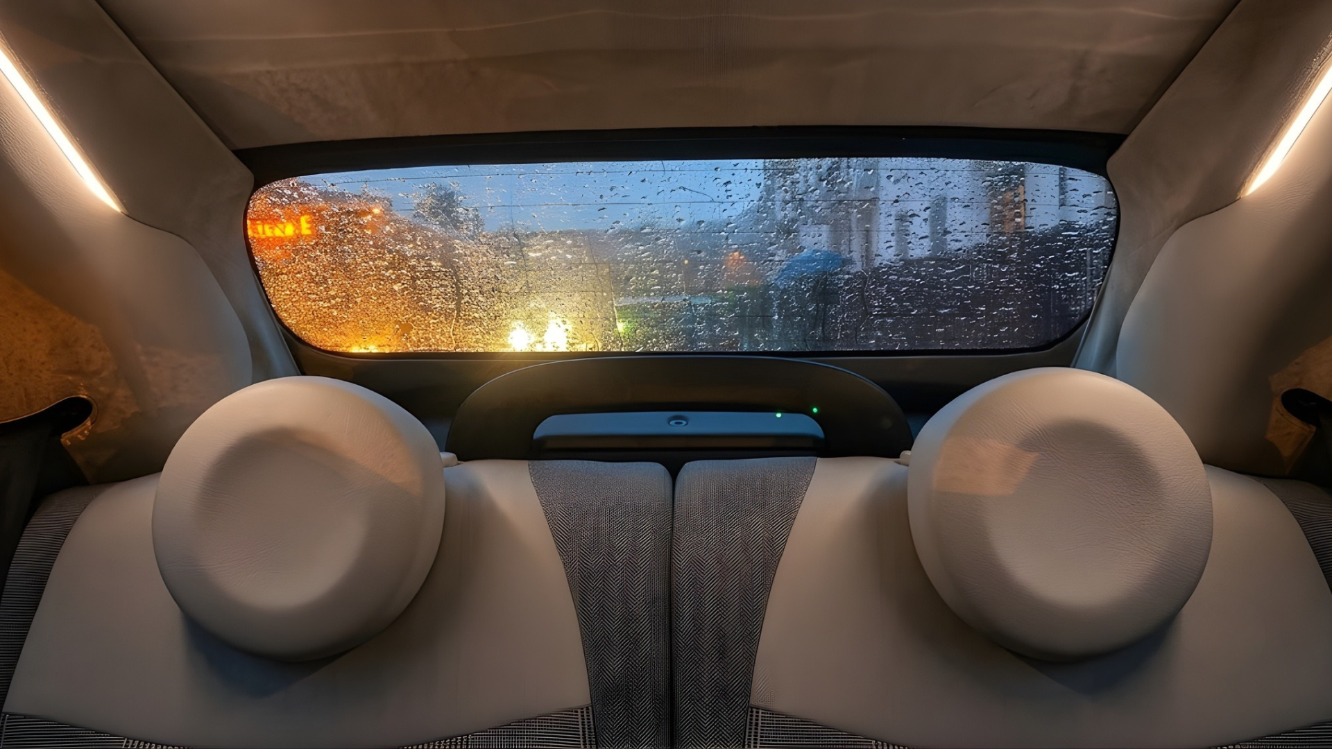 Back seat of a car with two beige headrests, looking out a rainy rear window at blurred city lights.