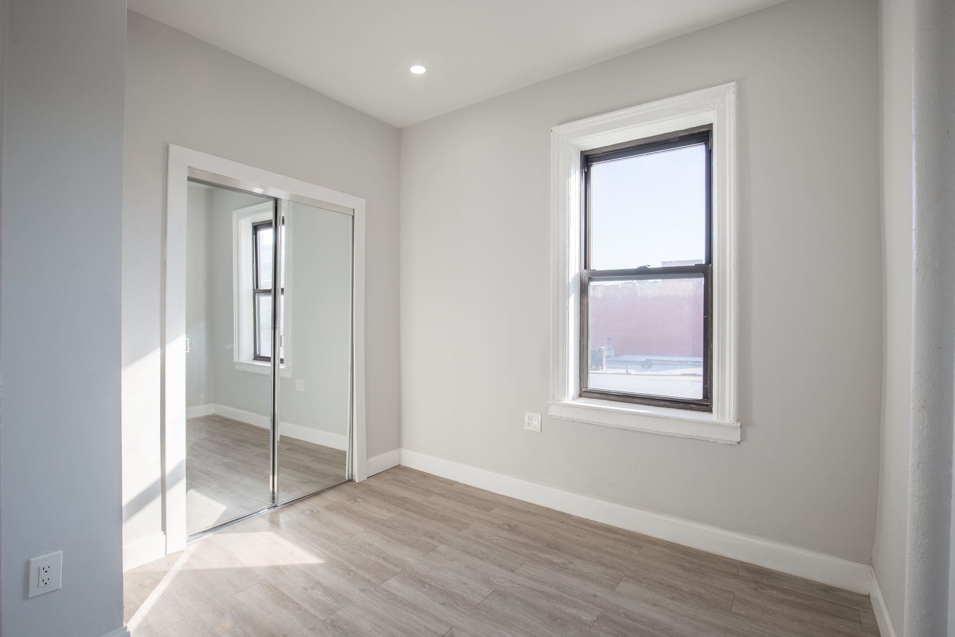 An empty room with a window and a mirrored door.
