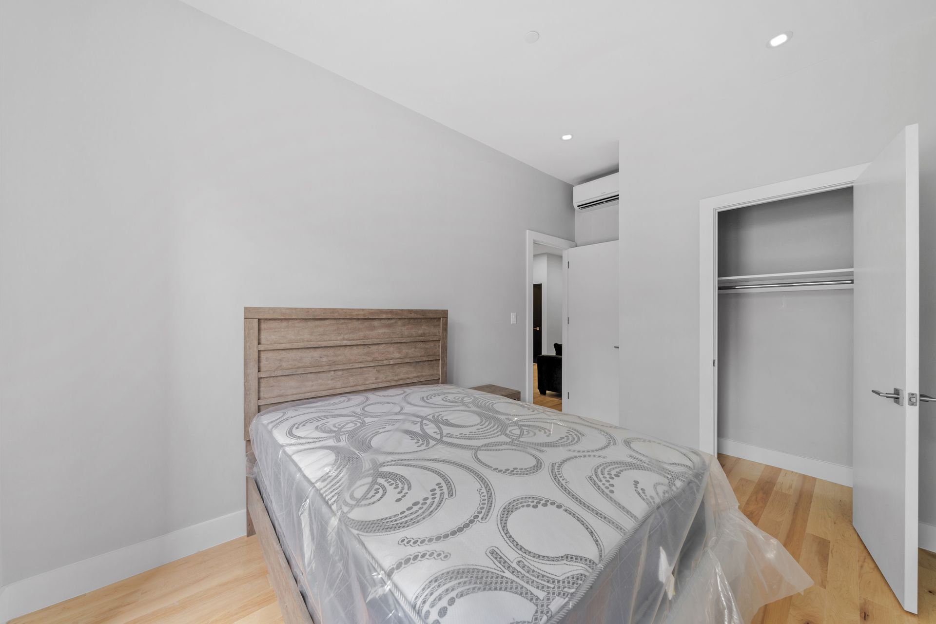 A bedroom with a bed and a closet with a mattress wrapped in plastic.