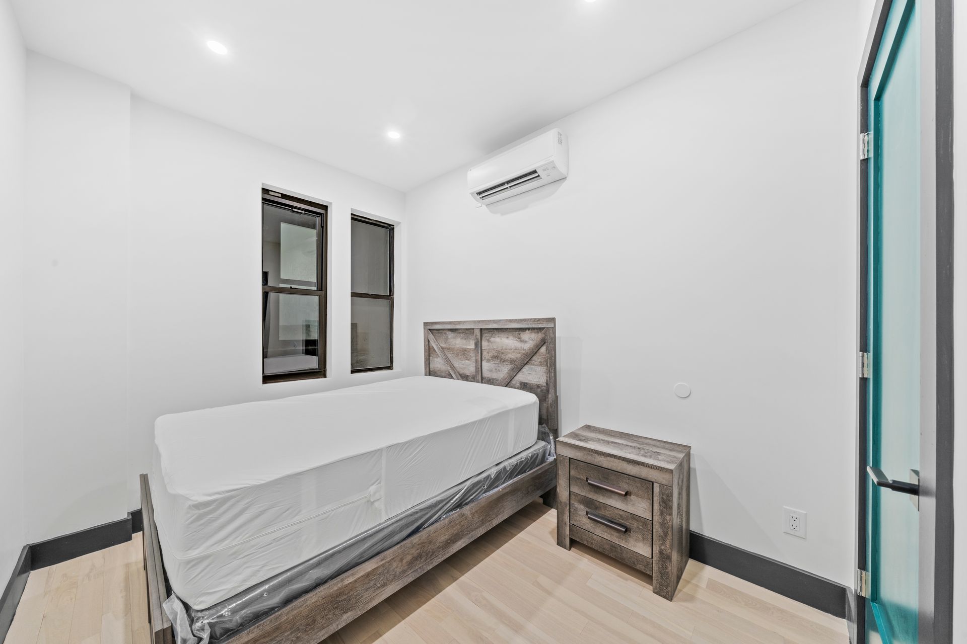 A bedroom with a bed , nightstand , and air conditioner.