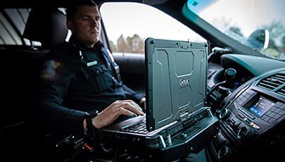 Police officer typing on a laptop inside his patrol car