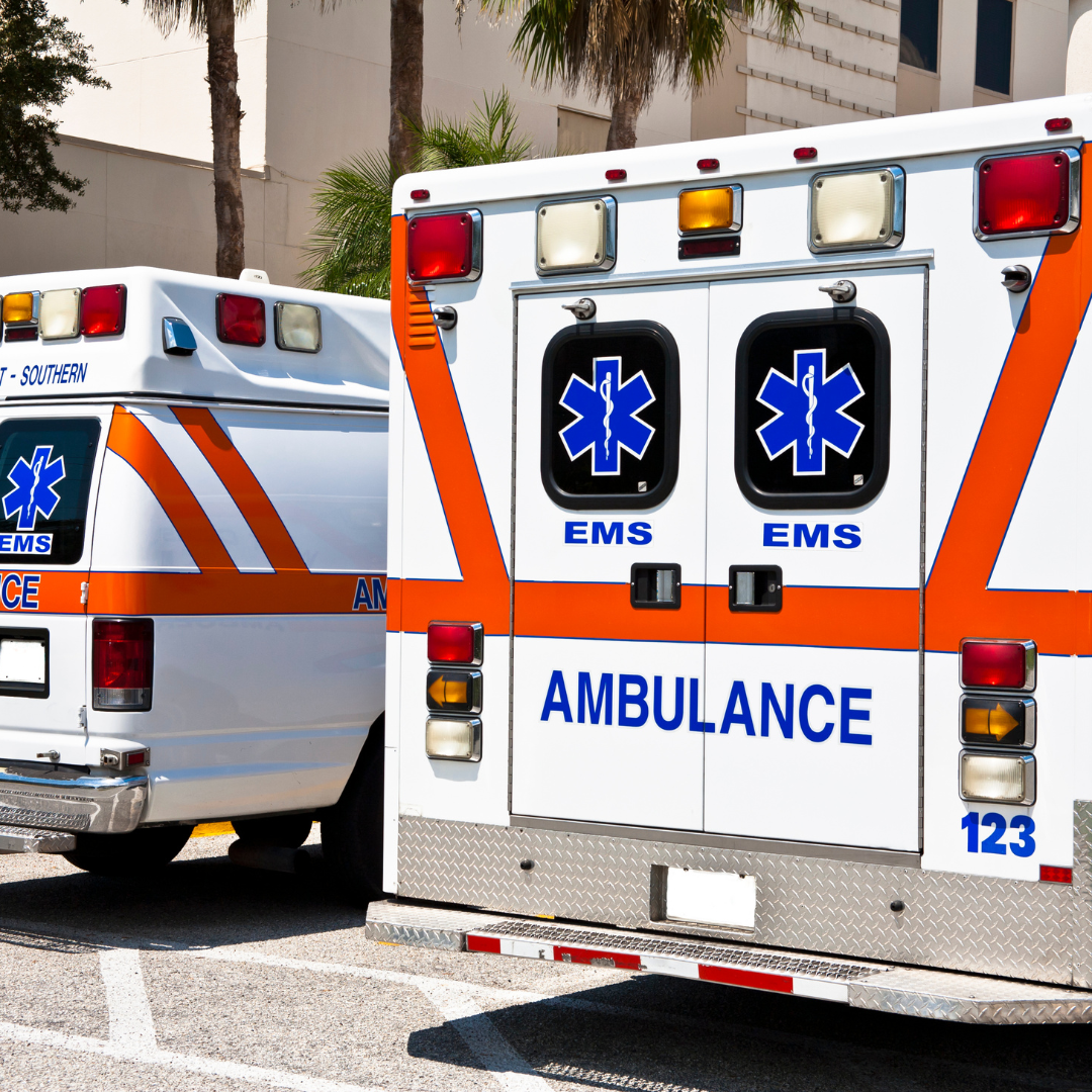 Two white and orange ambulances parked outdoors, rear doors facing the viewer