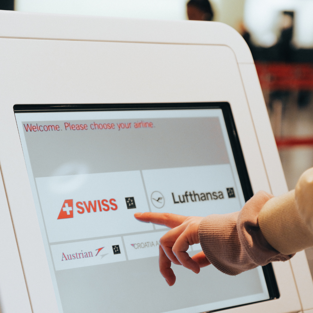 Hand selecting an airline on a kiosk touchscreen with SWISS and Lufthansa options