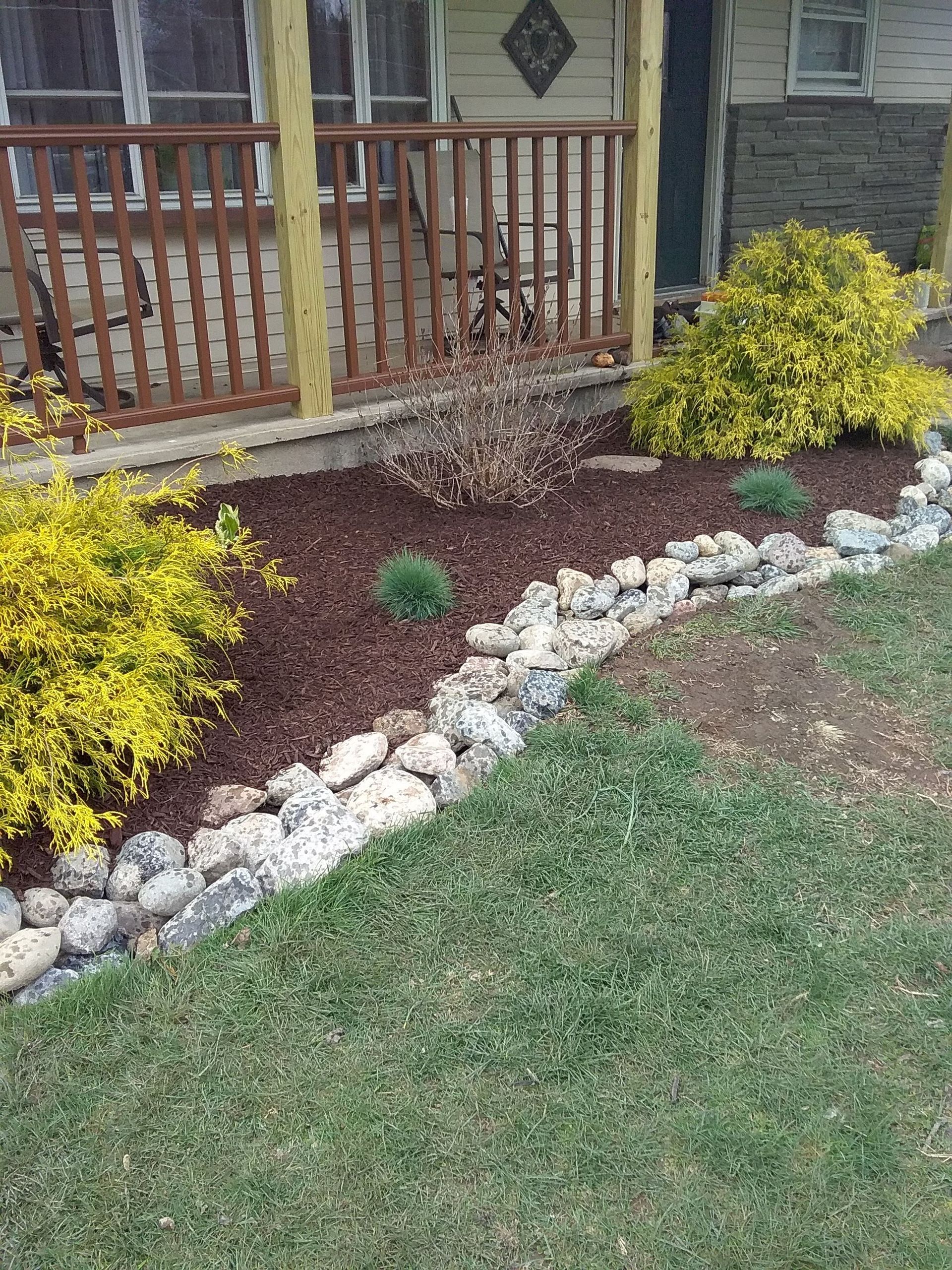 a house with a porch and a rock garden in front of it .