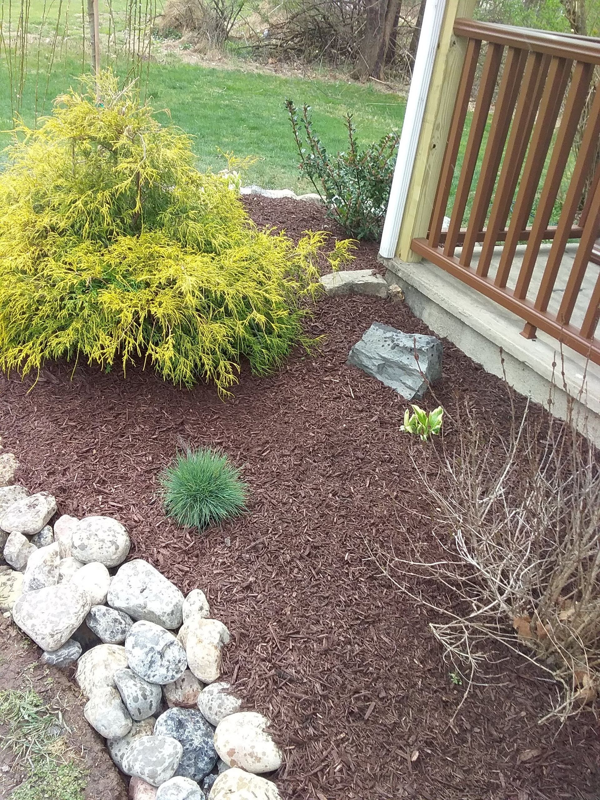 a garden with rocks and mulch next to a house with a railing .