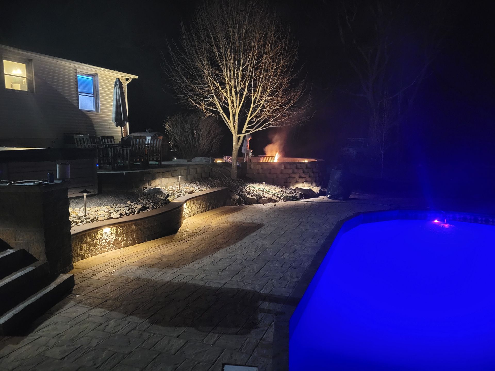 a swimming pool is lit up at night in front of a house .