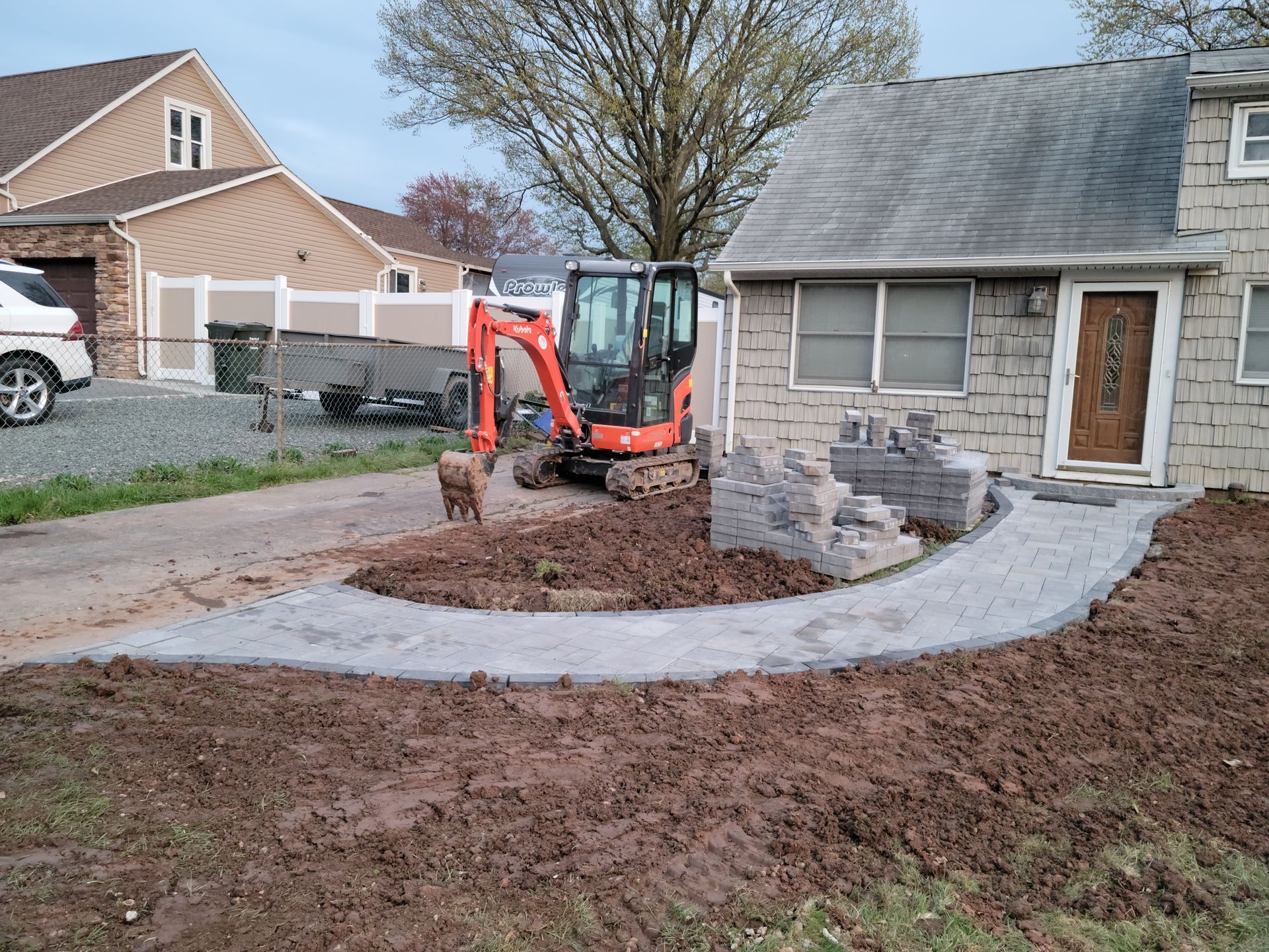 Construction site: Small excavator and brick walkway under construction at a house.