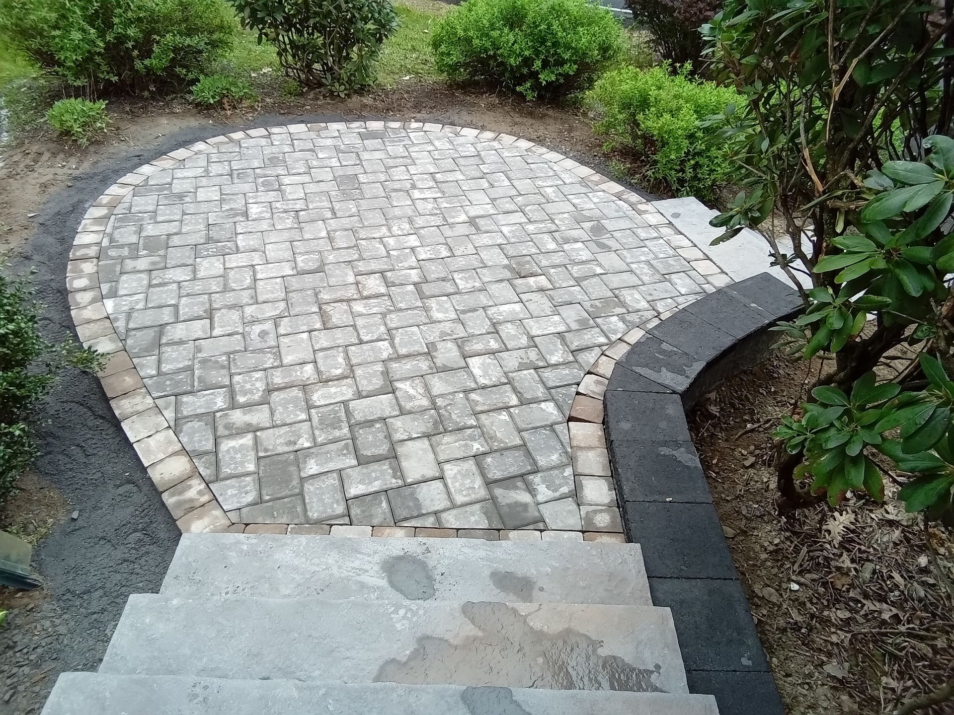 Stone patio with curved border, approached by steps, surrounded by greenery.