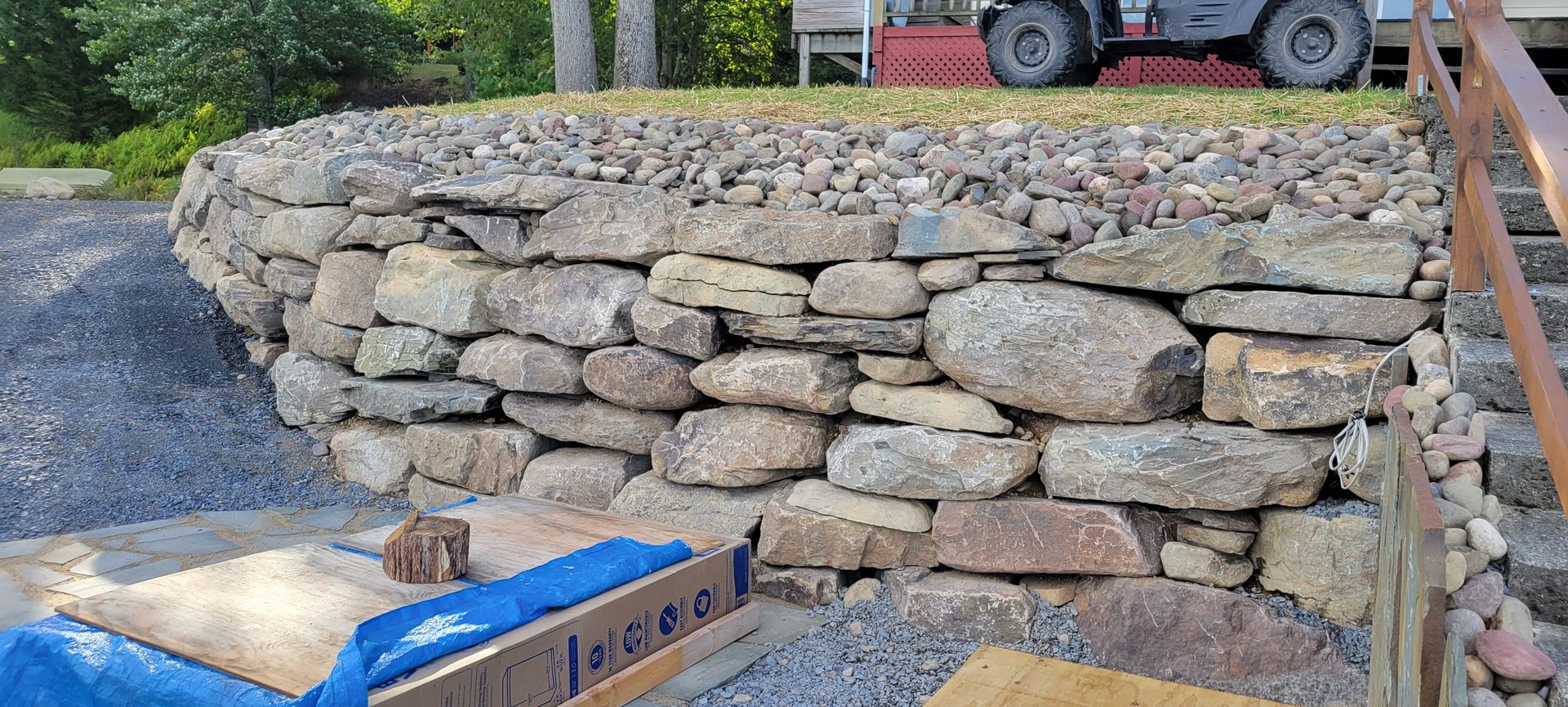a stone wall is being built in front of a house with a tractor in the background .