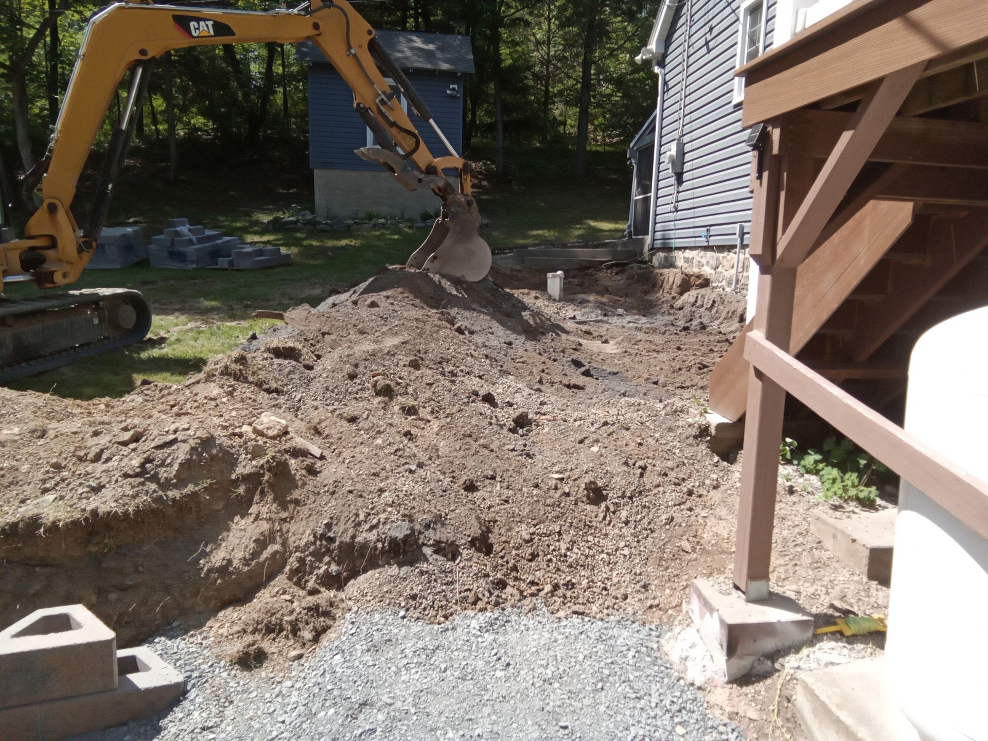 An excavator digging a trench beside a house. Pile of dirt and gravel visible.