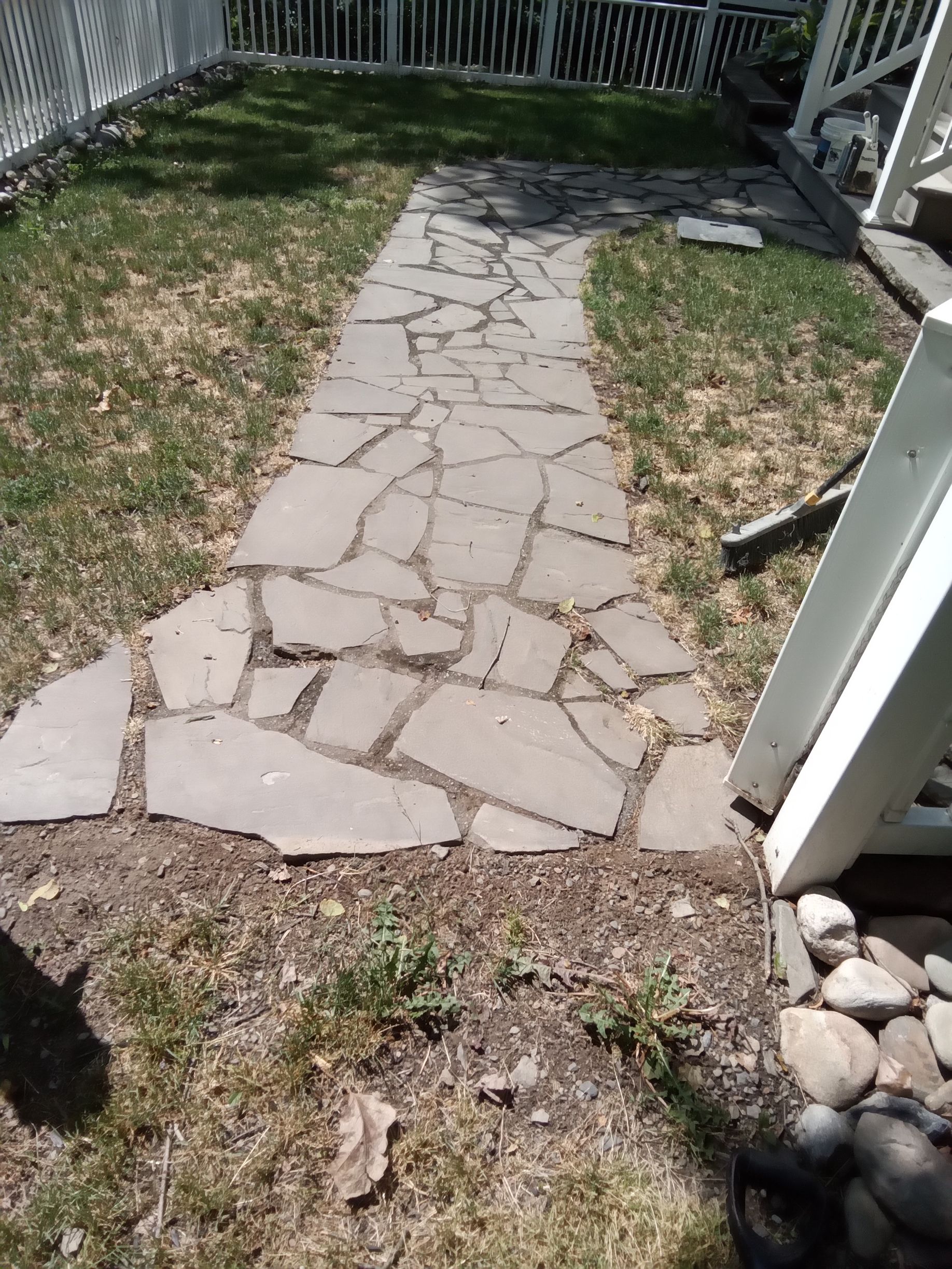 Stone path through a grassy yard, beside a white picket fence and a porch.