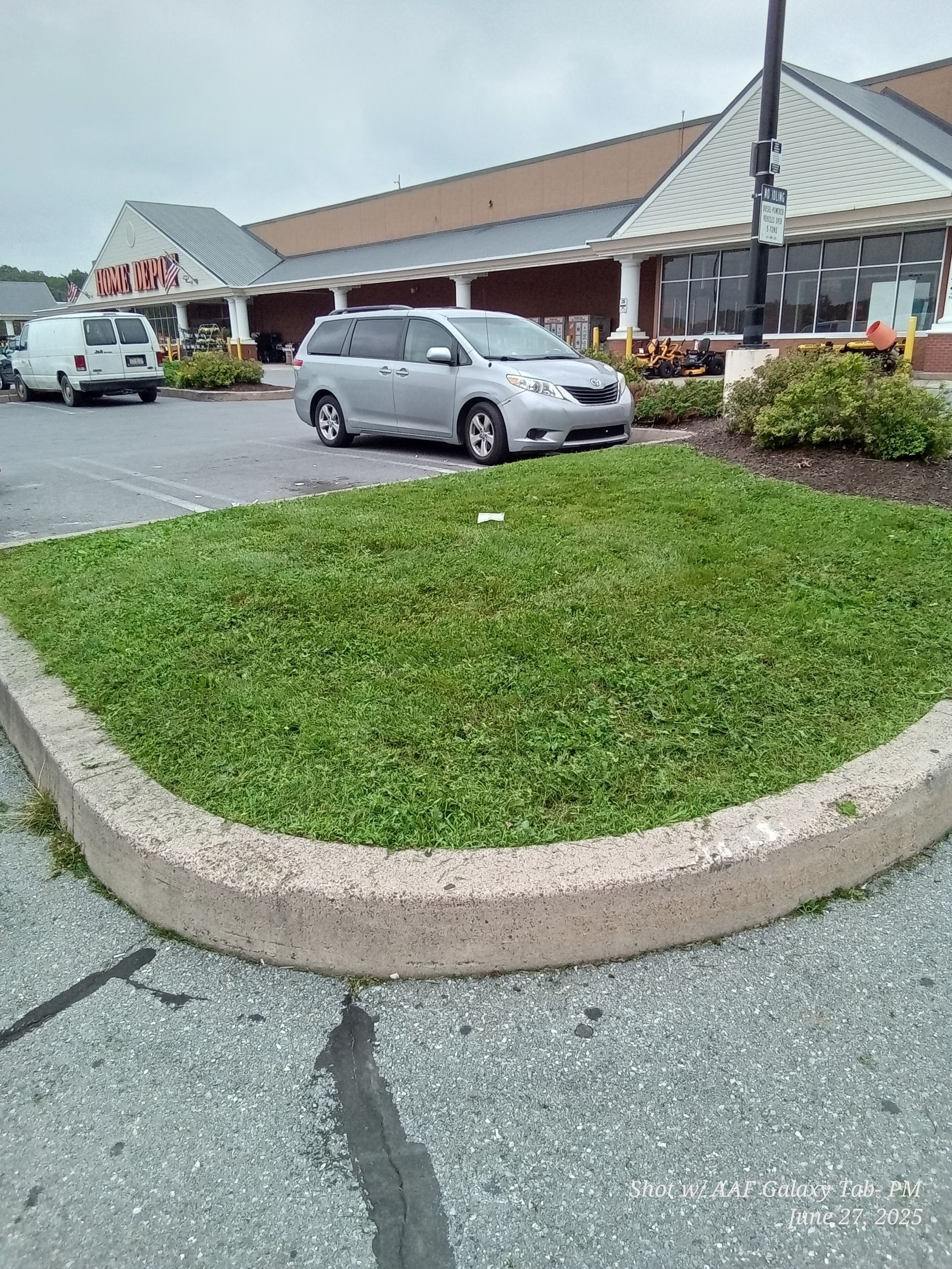 Silver minivan parked in front of a supermarket, with a green grassy area and a concrete curb in the foreground.