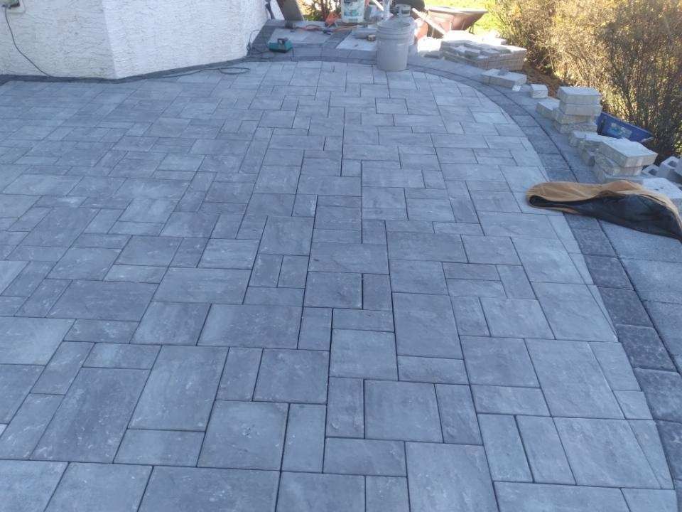 Gray brick patio with curved border, near a building and some landscaping.