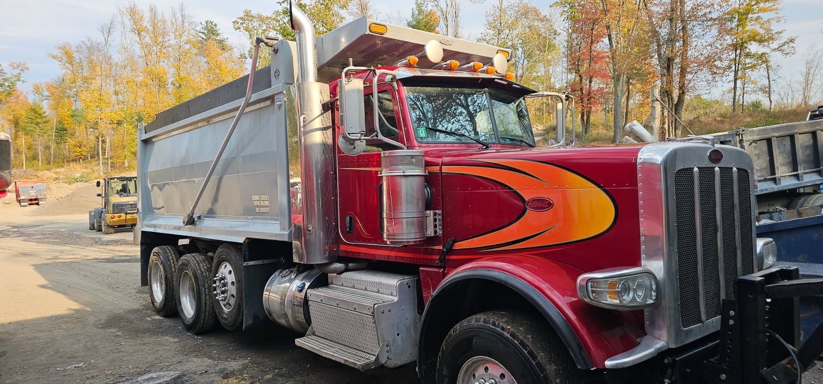 Red dump truck with a silver bed parked outside, autumn trees in the background.
