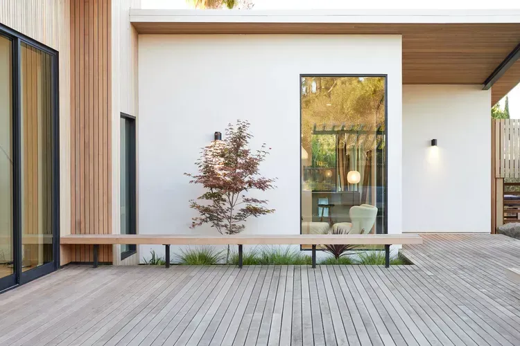 A white house with a wooden deck and a bench in front of it.