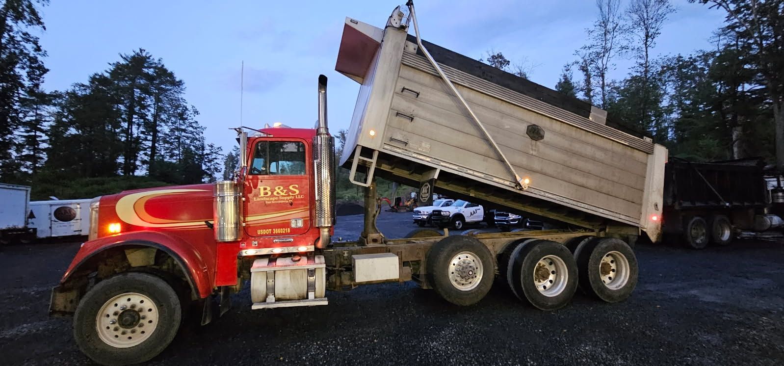 Red dump truck, with its bed raised, is parked outside, ready to unload.
