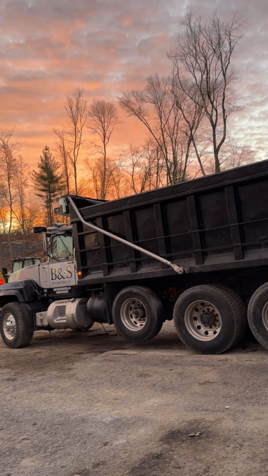 Dump truck with a raised bed against an orange and pink sunset.