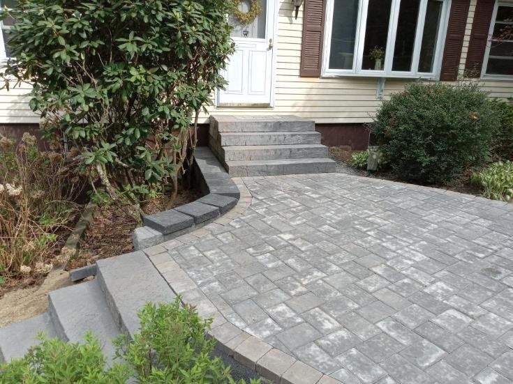 Gray paver walkway and steps leading to a house's front door with shrubbery.