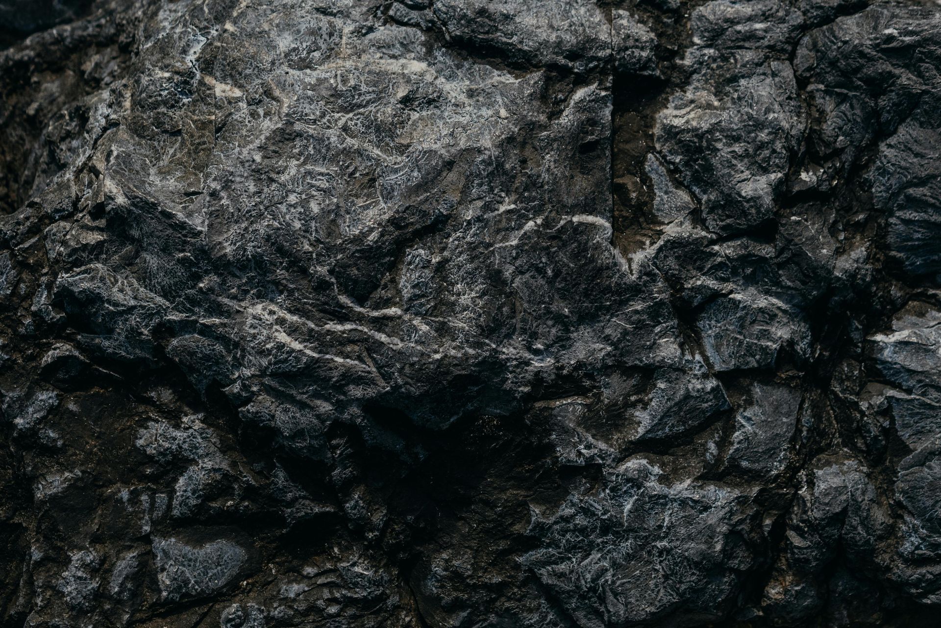 Textured close-up of dark grey rock formation with rough, jagged surfaces.