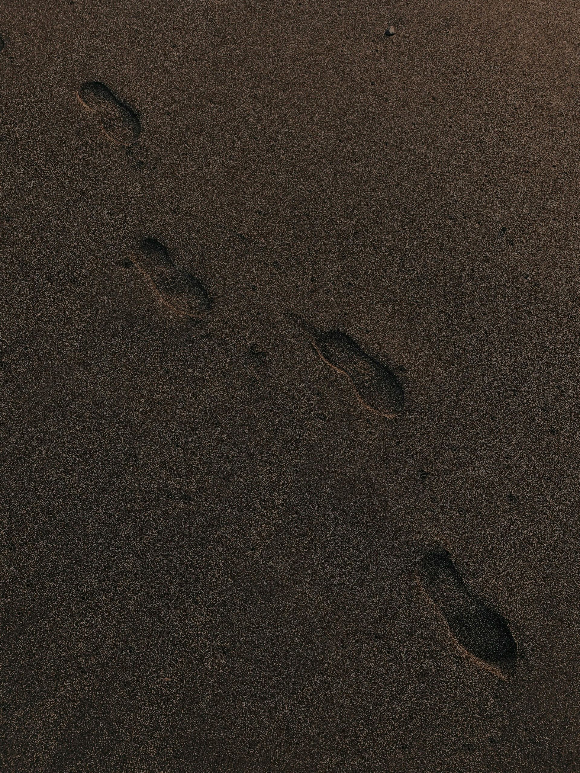 Footprints on dark, granular sand, leading diagonally upwards.