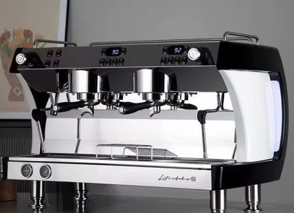 Cafetera espresso cromada con controles digitales y dos grupos de cabezales sobre encimera.