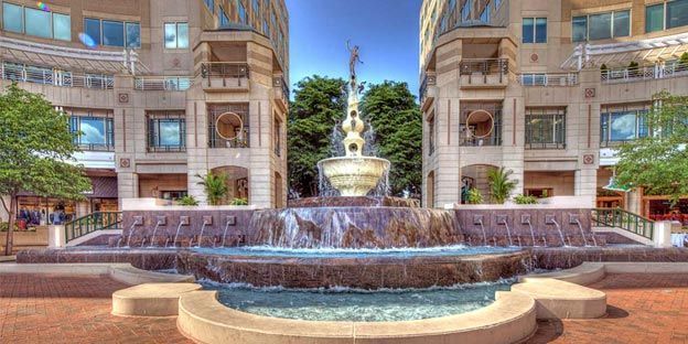 Courtyard fountain with cascading water between tan apartment buildings under a blue sky