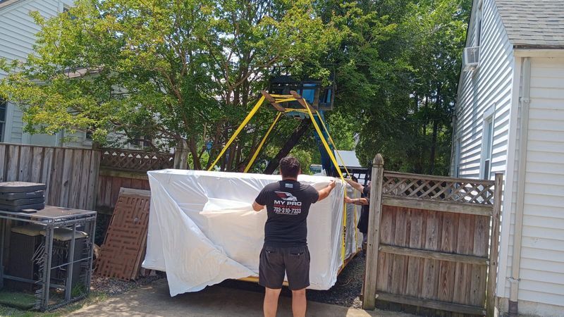 Person in a backyard adjusting a white tarp over a structure near a wooden fence and playset
