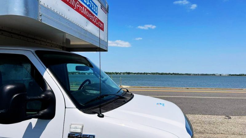 White box truck parked beside a wide blue body of water under a clear sky