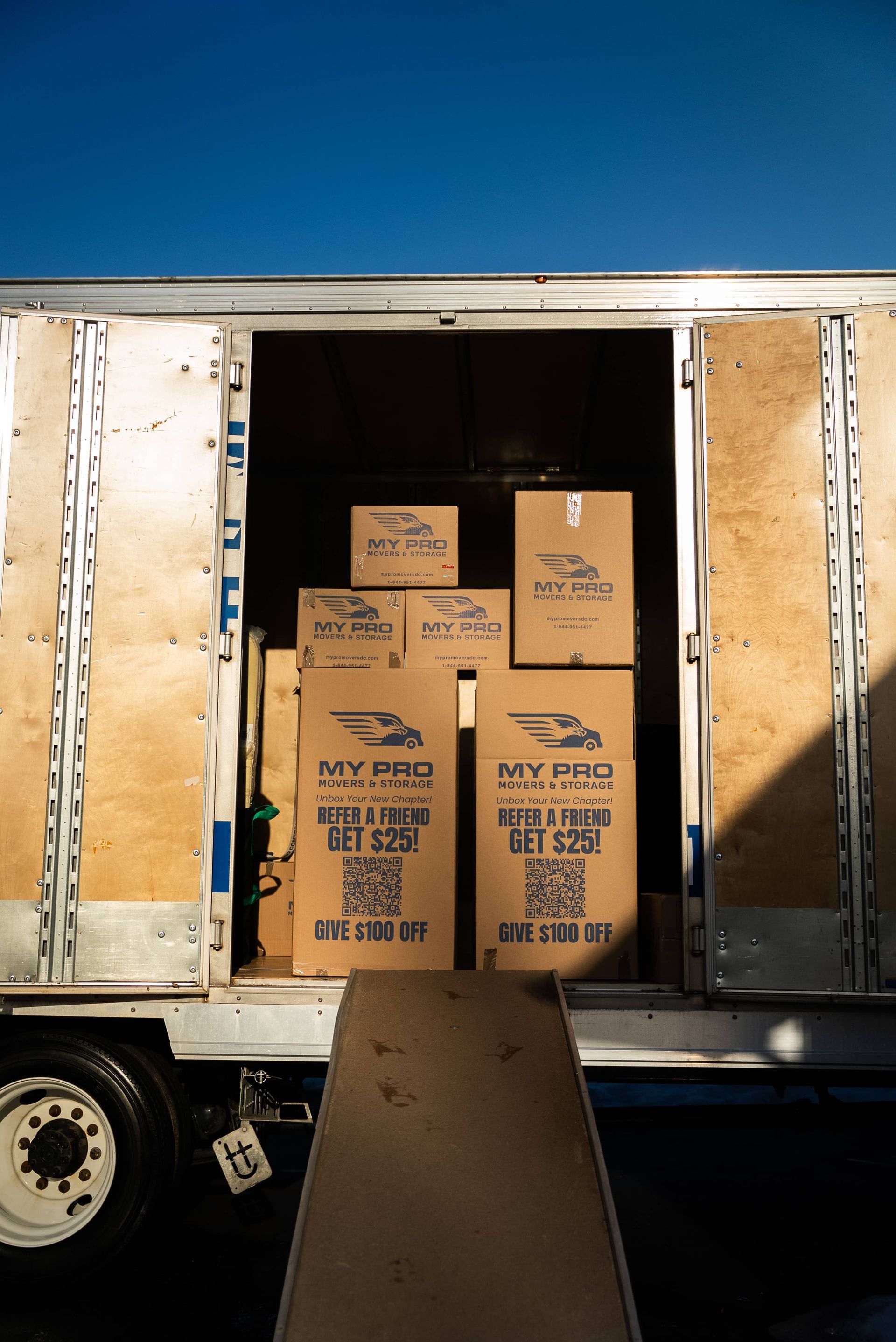Open box truck loaded with stacked cardboard boxes, viewed from the back in daylight.