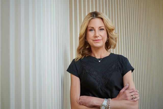 A woman in a black dress is standing with her arms crossed in front of a striped wall.