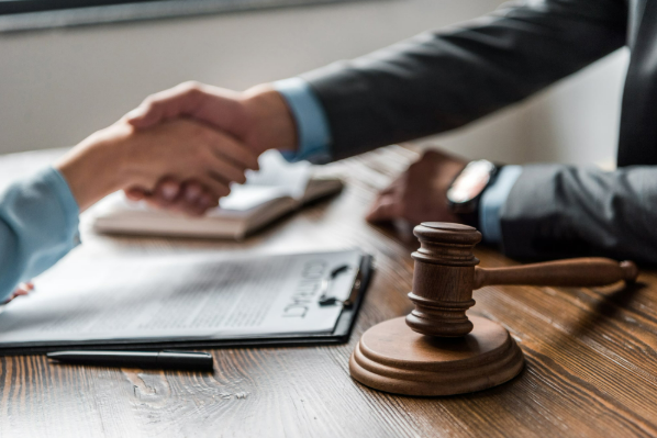 A man and a woman are shaking hands in front of a judge 's gavel.