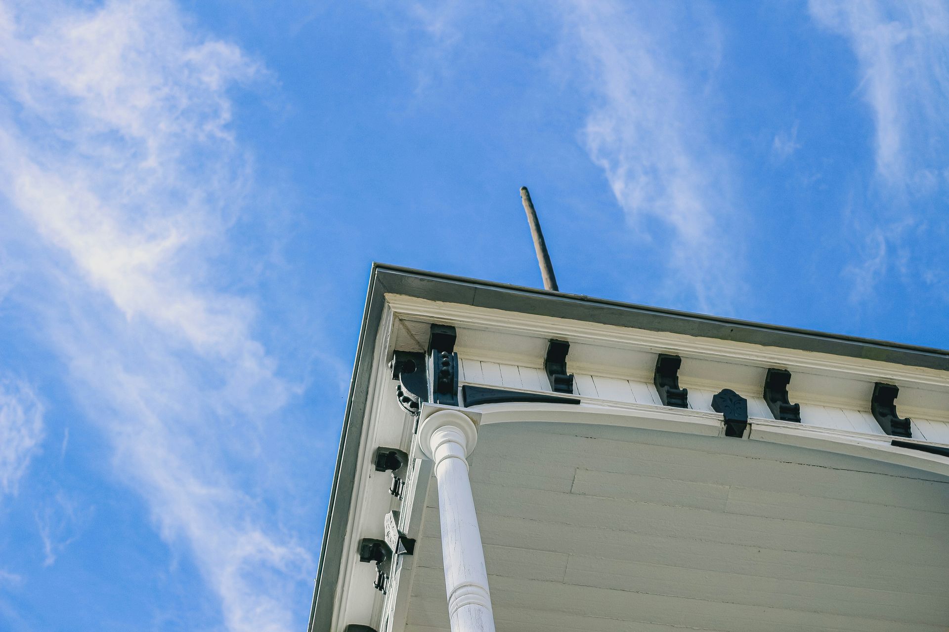 Close-up of a white house corner with roof trim against a blue sky with clouds