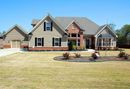 Suburban brick and beige house with a driveway, lawn, and landscaped front yard on a sunny day