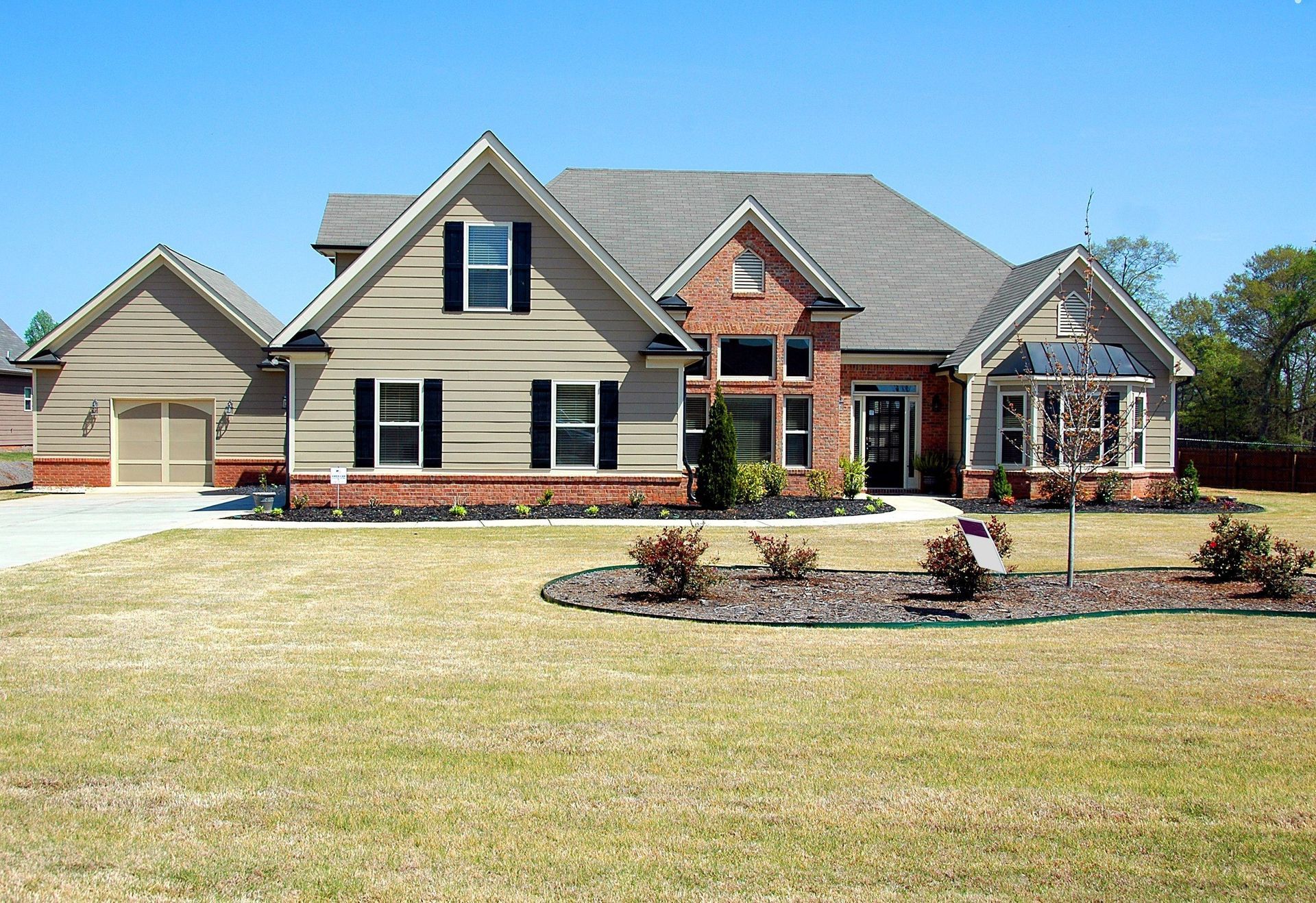 Suburban brick and beige house with a driveway, lawn, and landscaped front yard on a sunny day