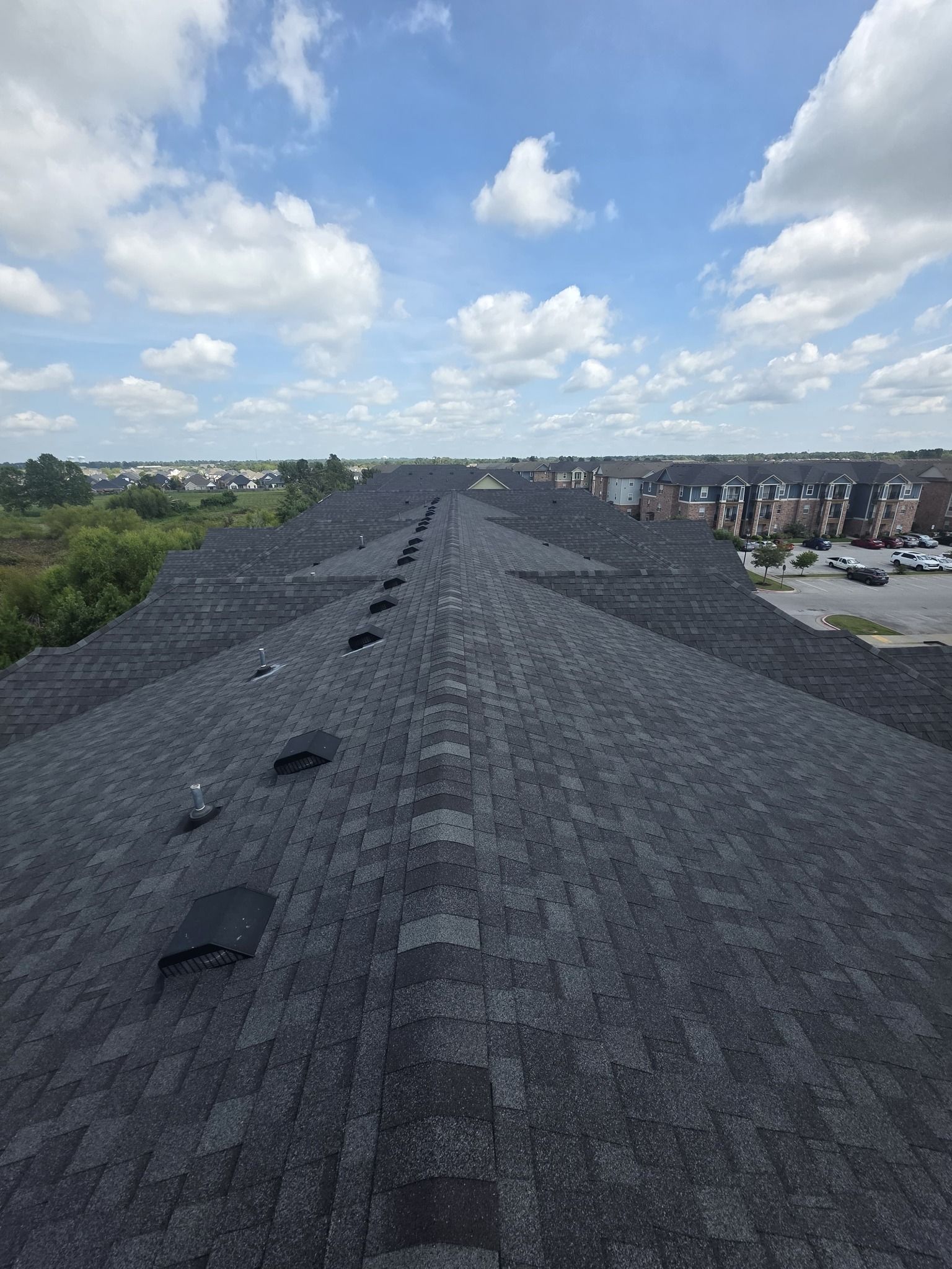 Rooftop with dark gravel under a cloudy sky, overlooking houses and trees in the distance