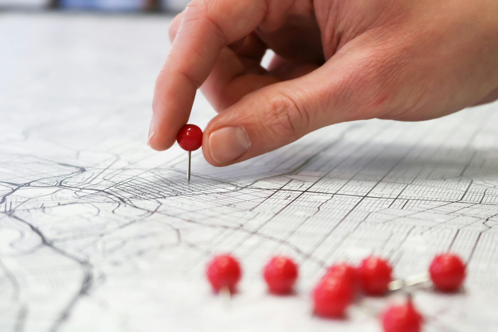 Hand placing a red pushpin on a map with several red pins nearby