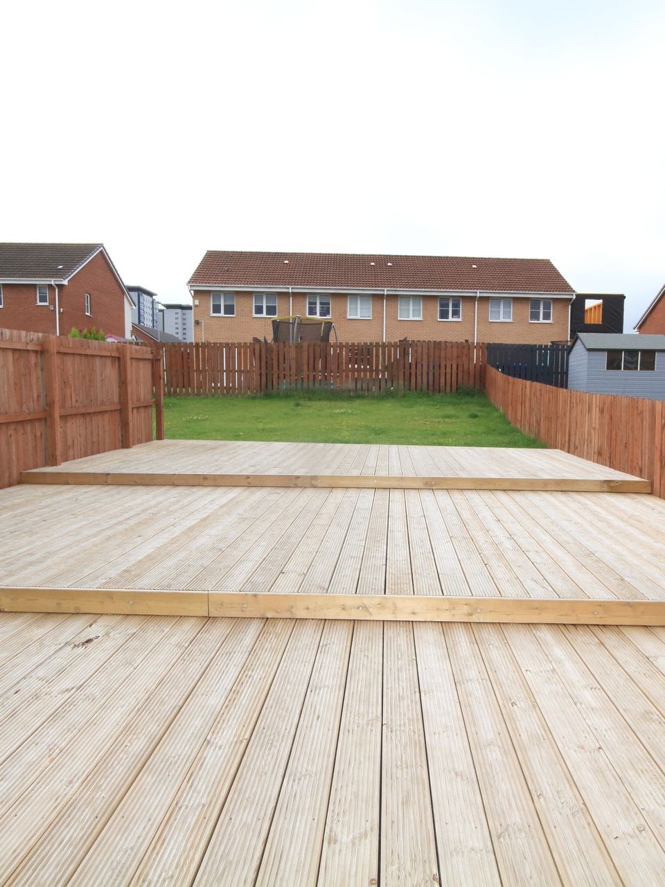 A wooden deck with a fence and a house in the background