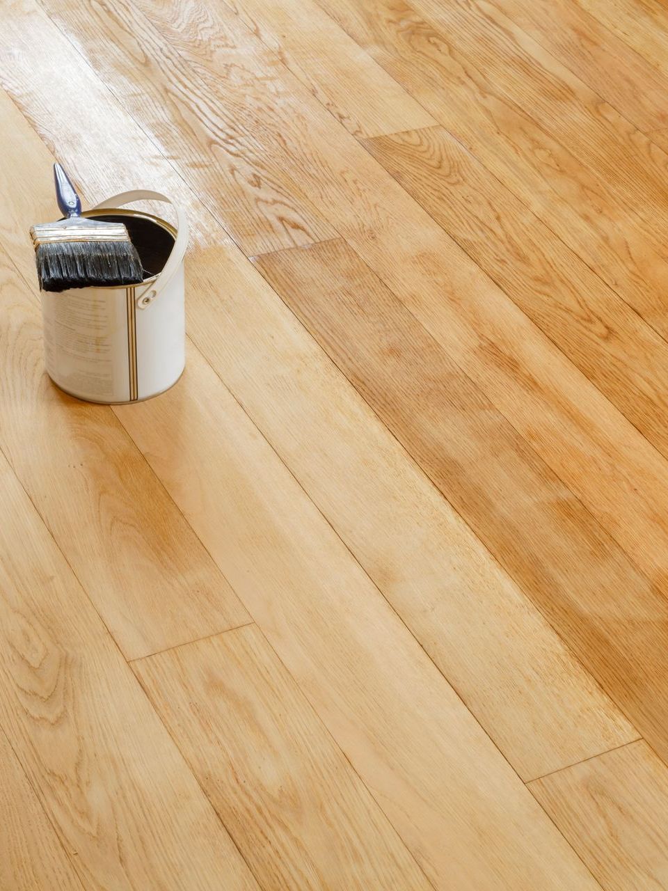 A can of paint and a brush on a wooden floor.