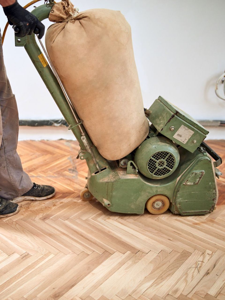 A person is sanding a wooden floor with a machine.