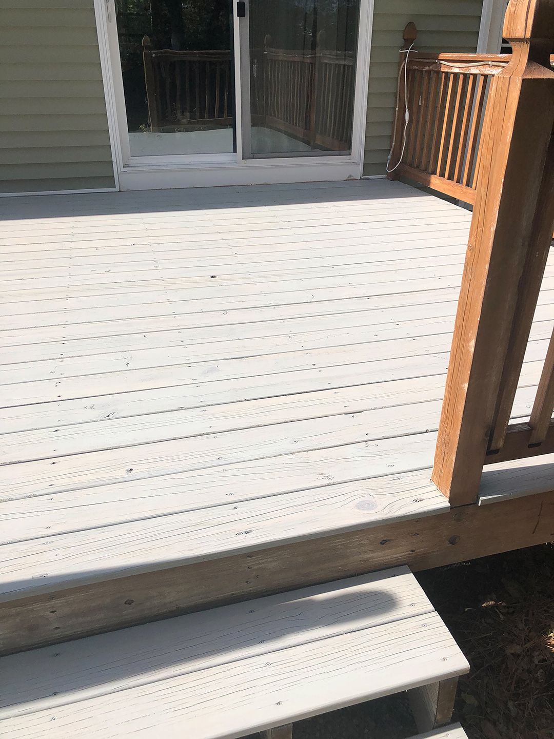 A white deck with a wooden railing and a sliding glass door.