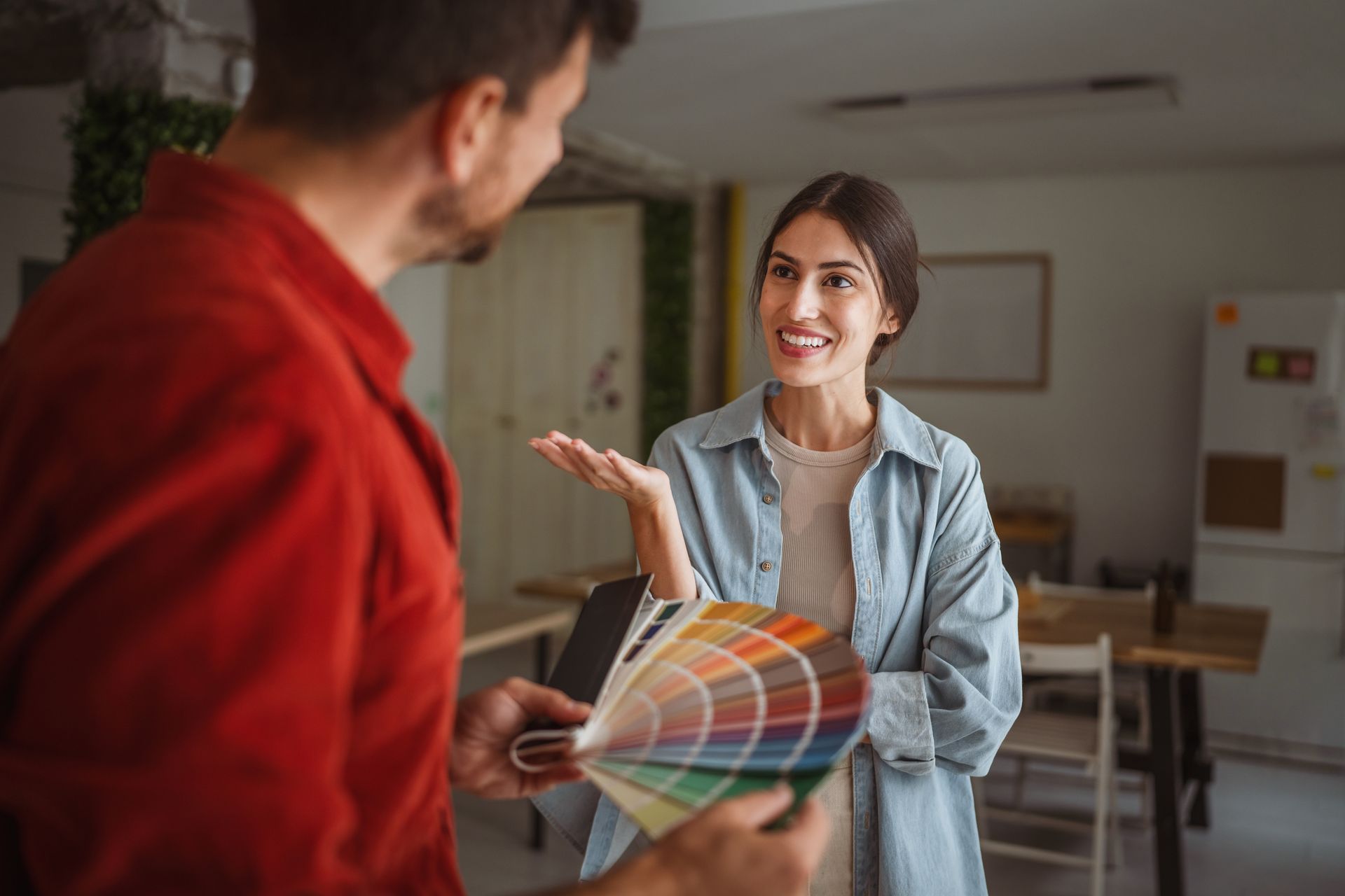Two people discuss color swatches in a bright room, with one smiling and gesturing toward the palette. Two people discuss color swatches in a bright room, with one smiling and gesturing toward the palette.